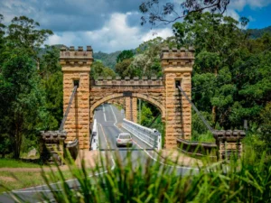 Hampden Bridge in Kangaroo Valley featuring the historic timber suspension bridge spanning the Kangaroo River surrounded by lush green countryside. The iconic heritage landmark is a must see attraction on a Kangaroo Valley family holiday.