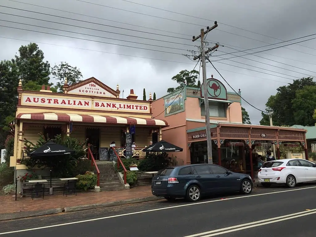 Kangaroo Valley High Street featuring heritage shopfronts with striped awnings leafy trees and rolling green hills in the background. The charming village atmosphere makes it a scenic stop on a Kangaroo Valley family holiday.