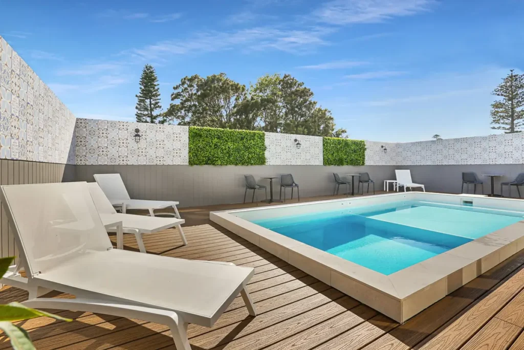 Nova Kiama rooftop pool featuring a modern plunge pool surrounded by white sun loungers and timber decking under a clear blue sky. The stylish coastal accommodation provides a relaxing base for a Kiama and Jervis Bay family holiday.