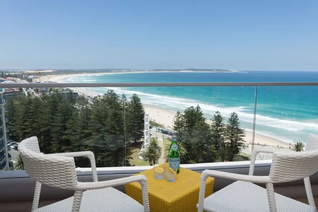 Balcony view from Rydges Cronulla overlooking a wide sandy beach turquoise ocean and pine lined foreshore along the Cronulla coastline. The beachfront location offers a convenient coastal base for a Royal National Park family holiday.
