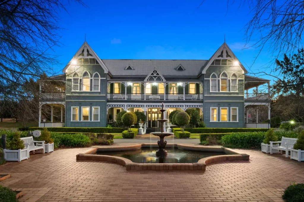 The Convent Hunter Valley featuring a grand two storey heritage mansion with ornate balconies manicured gardens and a central fountain at dusk. The elegant country estate offers boutique accommodation for a Hunter Valley family holiday.