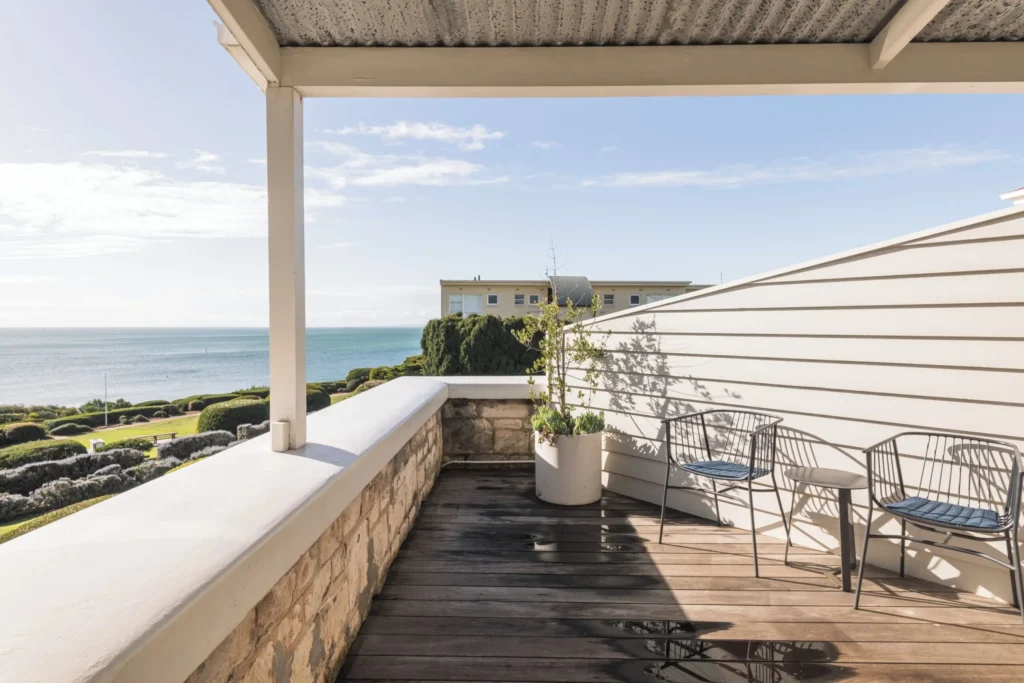 Private Hotel Sorrento balcony with two chairs overlooking manicured coastal gardens and calm blue water. The peaceful sea view creates a relaxing base for a Mornington Peninsula family holiday.