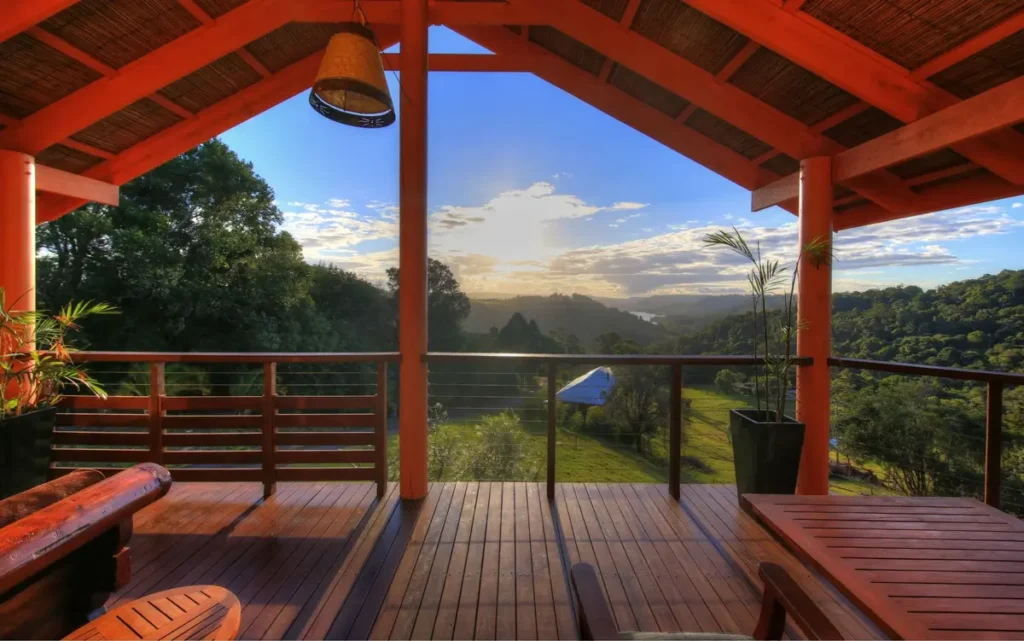 A timber deck with bold red beams looks out over rolling green hills and forest at sunset near Maleny. The peaceful hinterland view makes this a relaxing stay on a Sunshine Coast Hinterland family holiday.