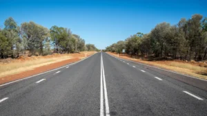 A wide red dirt road runs through dry outback landscape toward a large gateway sign in Charleville. The remote town setting captures the classic scenery families can expect on an outback Queensland family holiday.