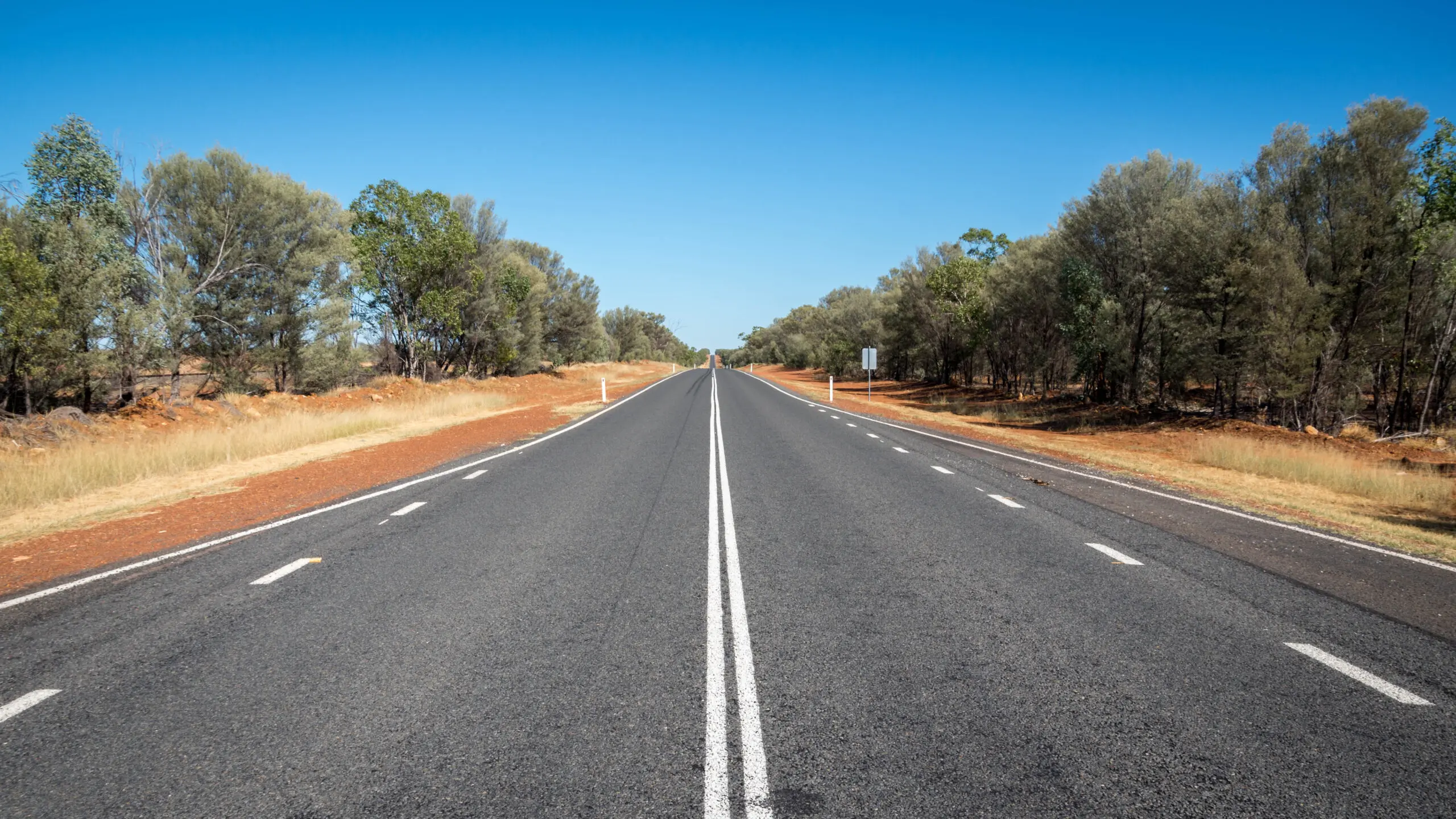 A wide red dirt road runs through dry outback landscape toward a large gateway sign in Charleville. The remote town setting captures the classic scenery families can expect on an outback Queensland family holiday.
