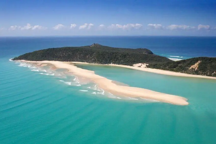 A long white sandbar curves through bright turquoise water beside a forested island under a clear blue sky. This coastal scenery shows the kind of island landscapes families can explore on a Fraser Island family holiday.