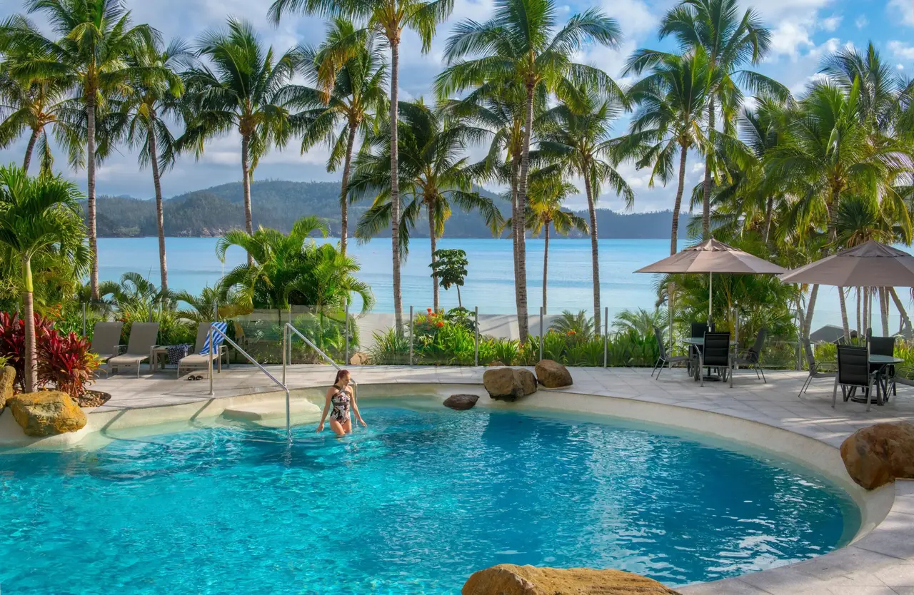 a woman in a pool with palm trees and a body of water