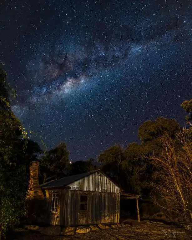 A rustic timber cabin at Diamondvale Estate sits among trees beneath a bright Milky Way sky. The peaceful night setting shows the kind of quiet country escape families can enjoy on a Southern Downs and Granite Belt family holiday.