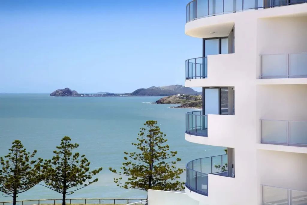 Oshen Apartments Yeppoon has curved white balconies overlooking the ocean, pine trees, and distant rocky islands. The coastal apartment setting offers a scenic place to stay during a Capricorn Coast family holiday.