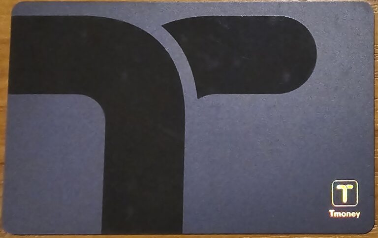 A Tmoney card with a minimalist black and gray design, featuring a stylized "T" logo in the bottom right corner. The card is used for public transportation payments in South Korea.