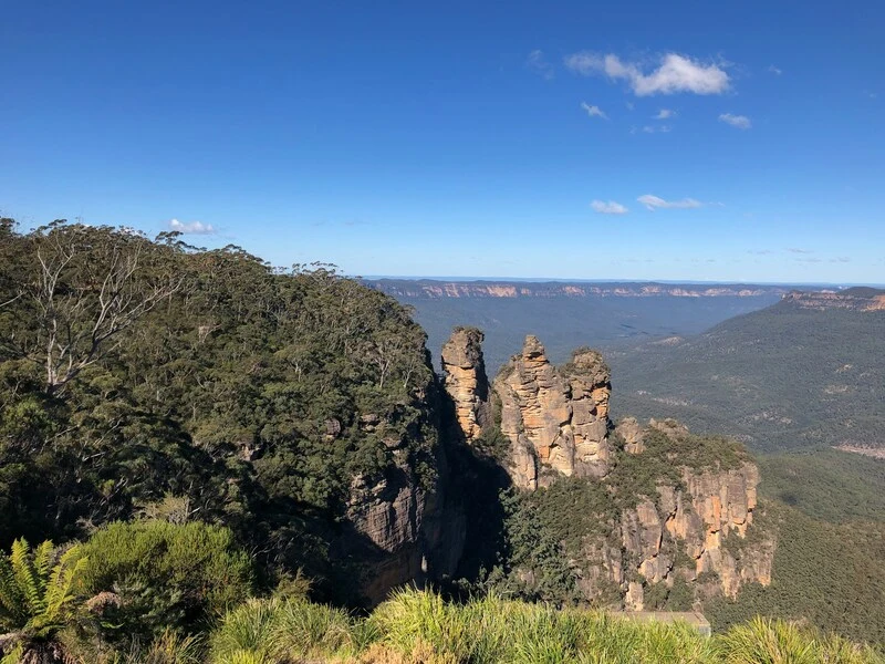 The iconic Three Sisters rock formation rises above a lush forested valley in the Blue Mountains, offering a breathtaking view for those planning how to see more of NSW.