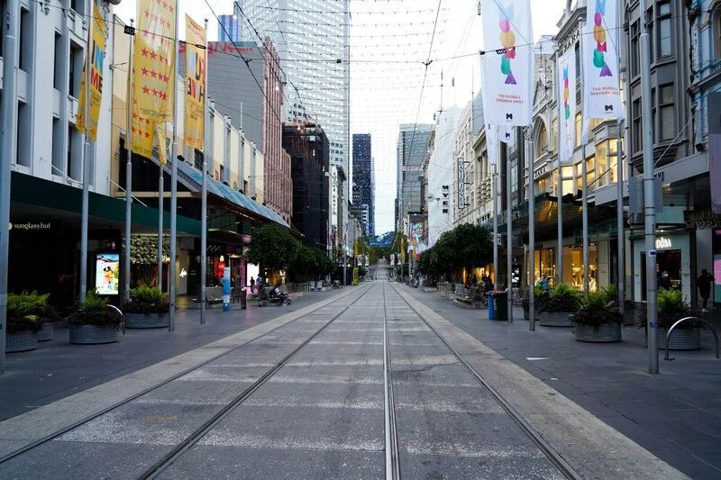Bourke Street Mall in Melbourne with tram tracks running down the center between shops and cafes. Decorative banners hang overhead while pedestrians sit along the wide walkway in the early evening. This scene shows the walkable city core that makes the Best Way to See Victoria on a Short Trip efficient and convenient.