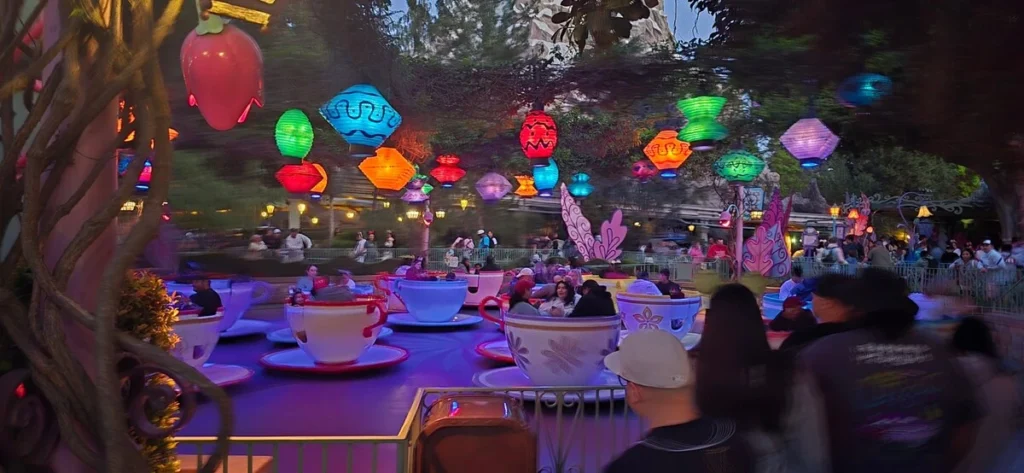 Mad Tea Party teacup ride at Disneyland glowing with colorful lanterns and spinning cups at dusk. Families and visitors enjoy the vibrant nighttime atmosphere of the popular attraction.