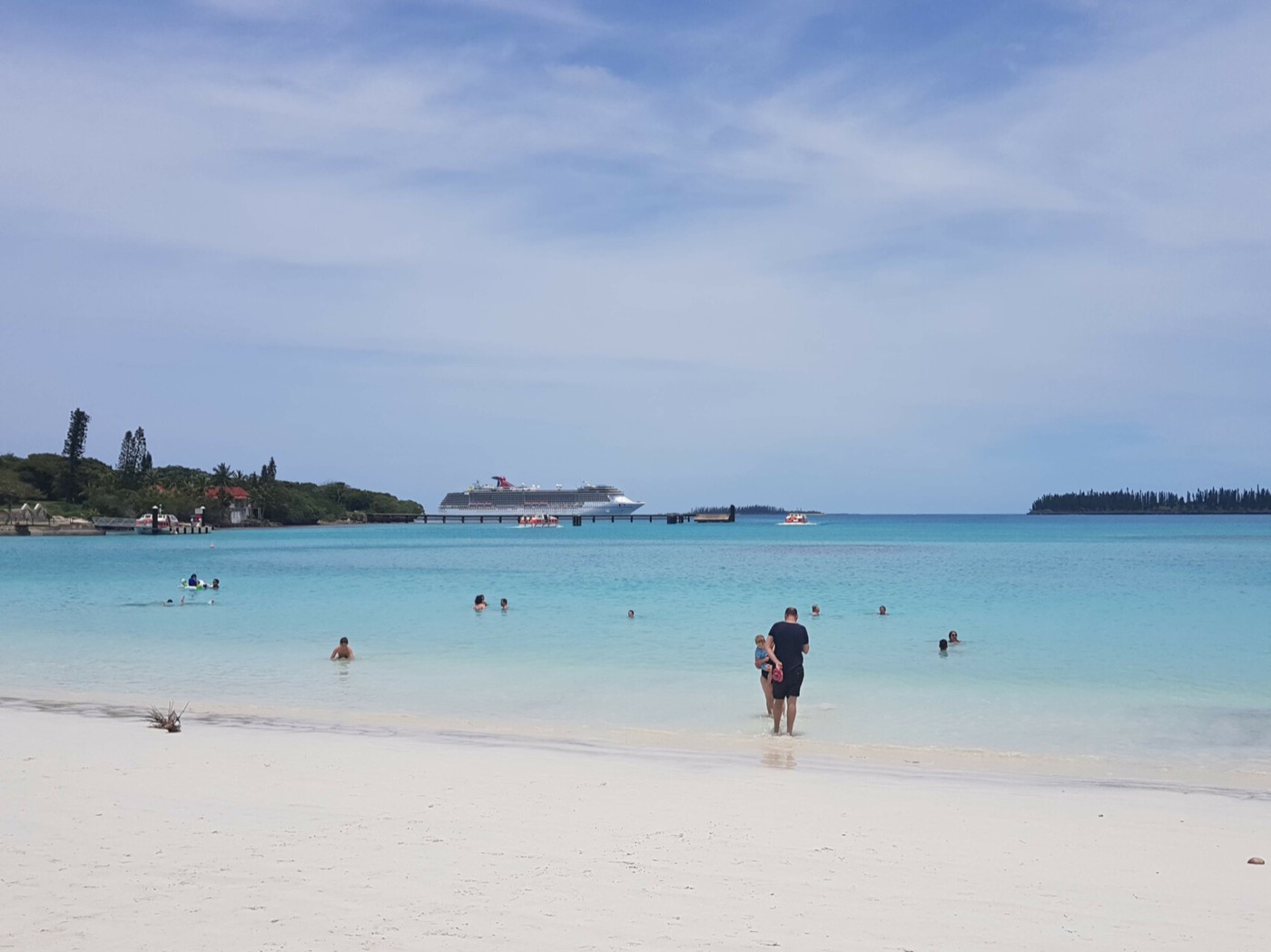 Family swimming at a South Pacific island beach with a Carnival cruise ship at the pier