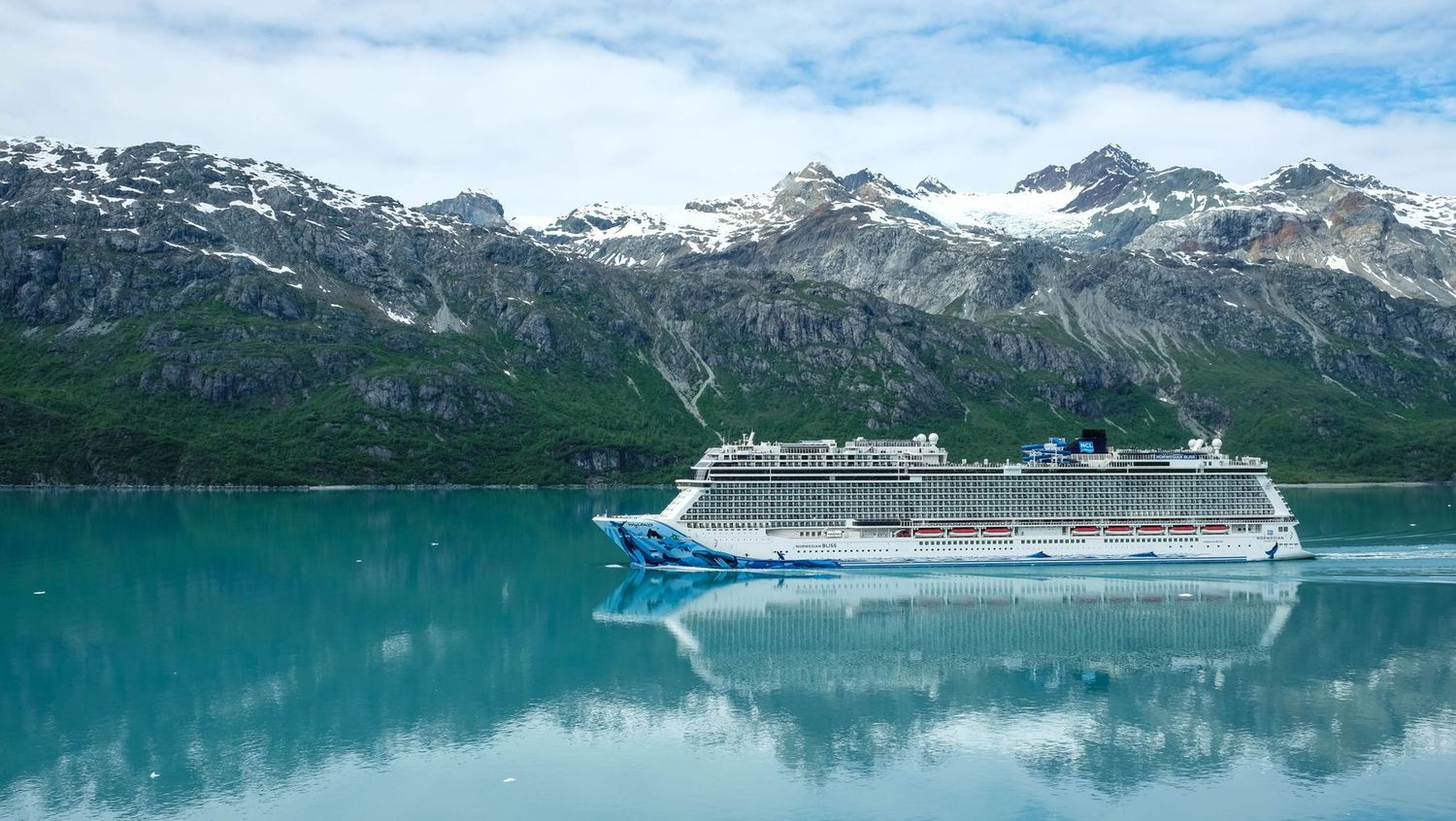 Large cruise ship sailing past snow-capped mountains in an Alaskan fjord