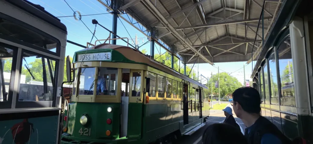 Vintage green Bendigo tram displaying "JOSS HOUSE" at a covered tram depot with passengers waiting nearby. Riding the heritage tram is a family friendly way to explore the city on a Bendigo family holiday.