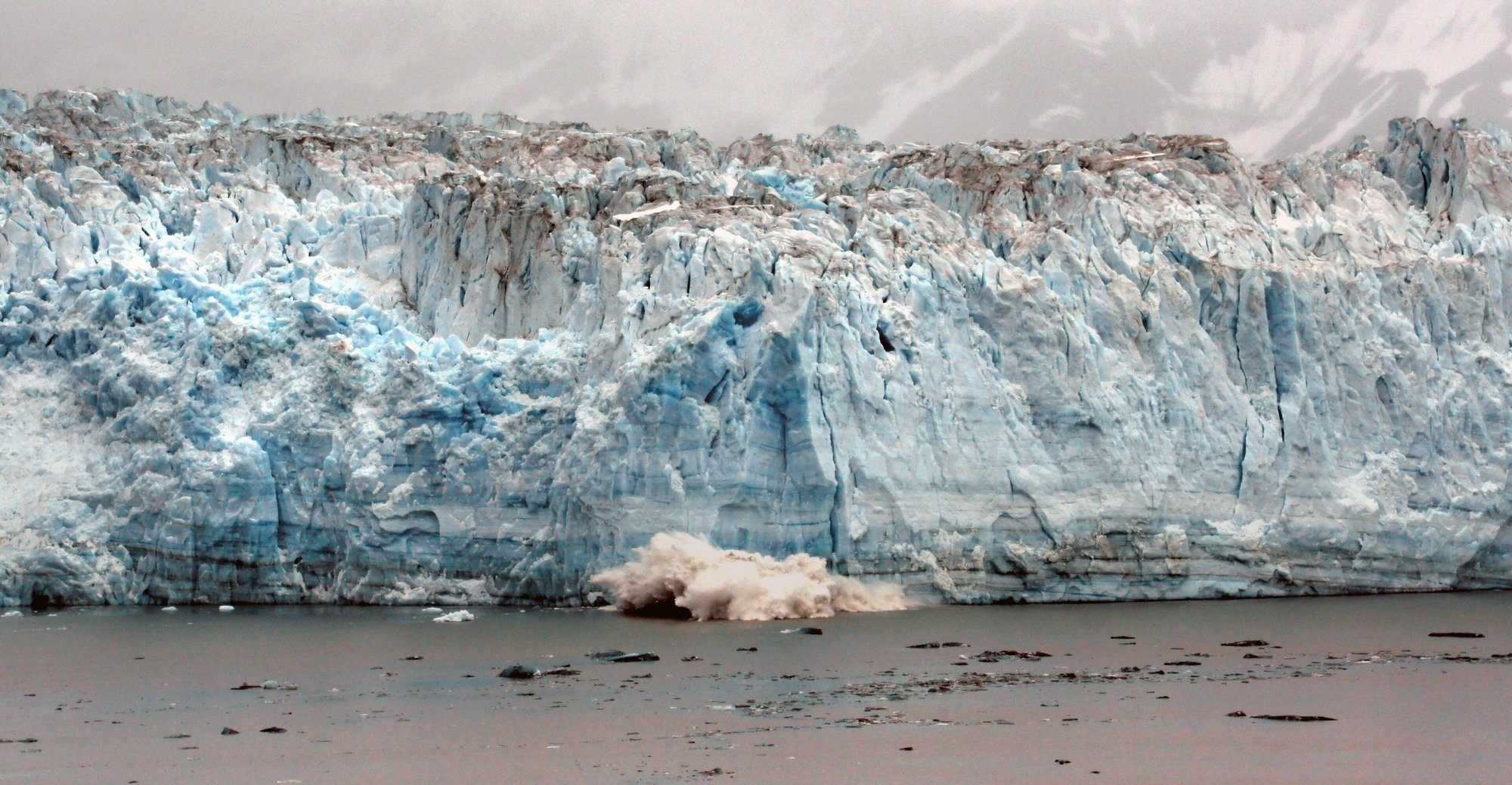 Large cruise ship sailing past snow-capped mountains in an Alaskan fjord