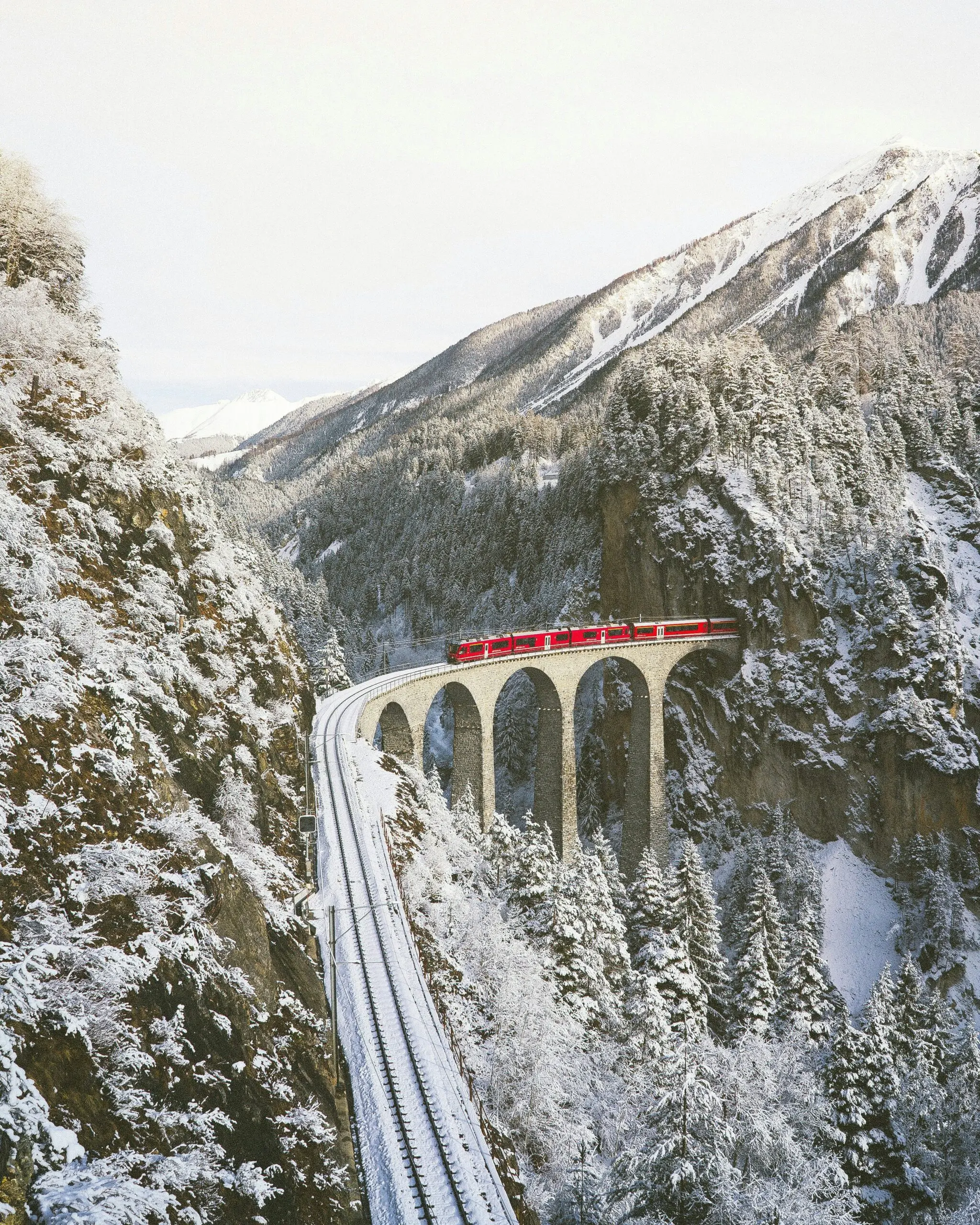 Red train crossing a snowy mountain viaduct in Switzerland